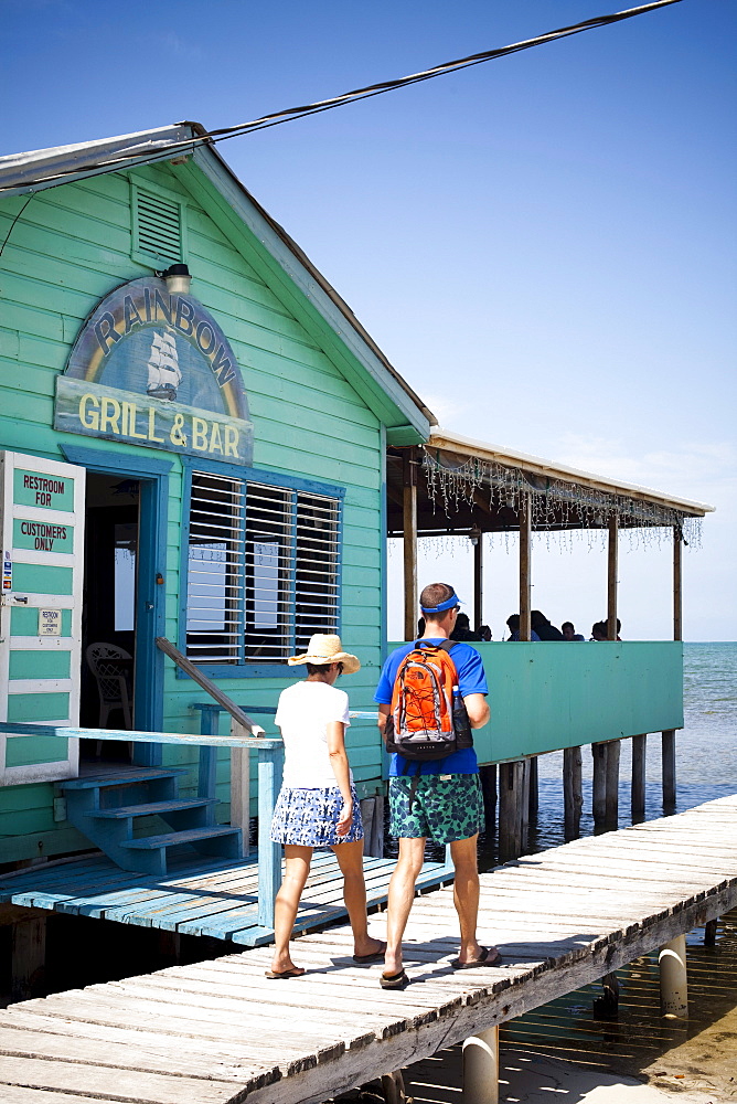 A couple walk down a dock near a ocean side restaurant.