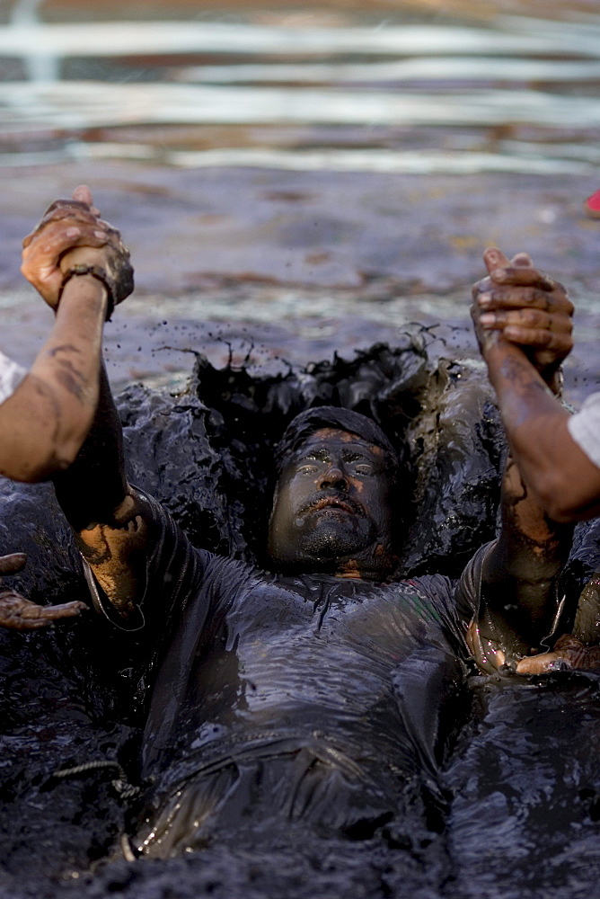 A man is baptized in the healing mud of Espinoza, Mexico.Twice a year the faithful visit Espinazo, a small dusty village and birthplace of El Nino Fidencio, one of the most revered healers in North East Mexico.  Although he died in the 1940s people believe certain priests known as Materias can channel his healing gifts and cure people.  During the anniversary of his birth and death over 100,000 people take part in the celebration by giving thanks at his gravesite or bathing and getting healed in mud baths.