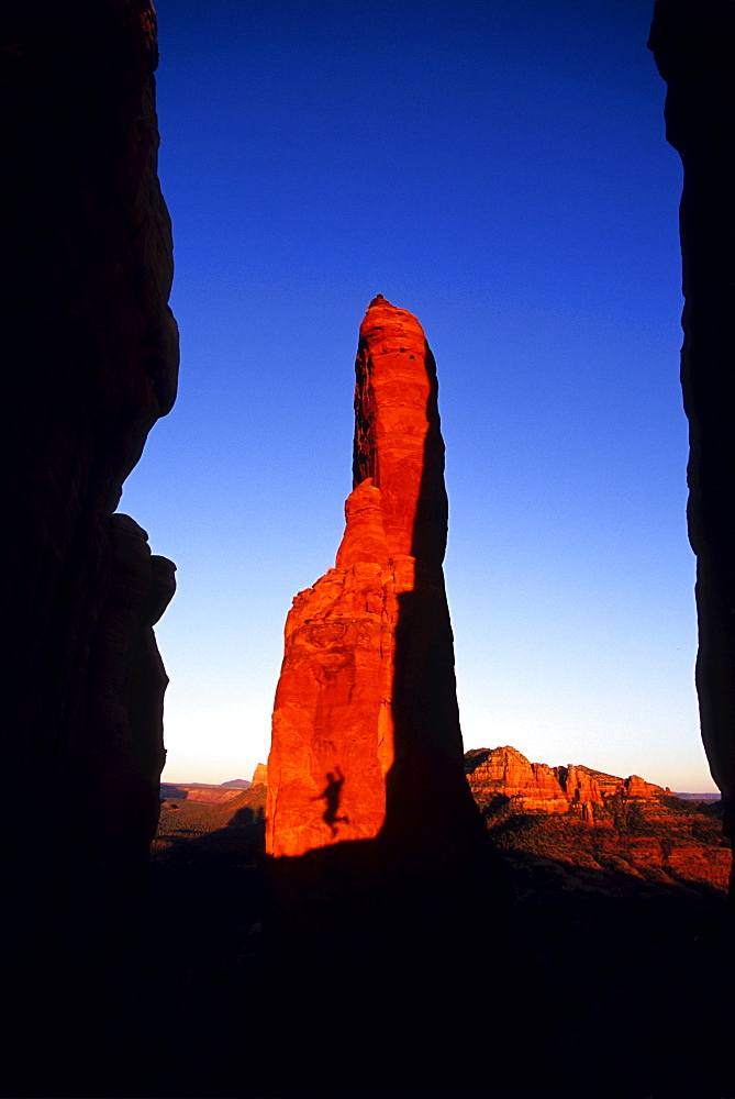 A person's shadow caught in mid-jump on a red rock spire in Sedona, Arizona, at sunset.