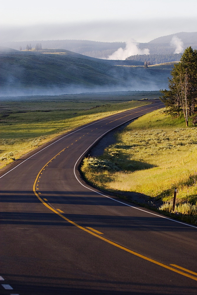 A road winds through the grasses of Hayden Valley in Yellowstone National Park, Wyoming on July 24, 2005 as mist rises in the background.