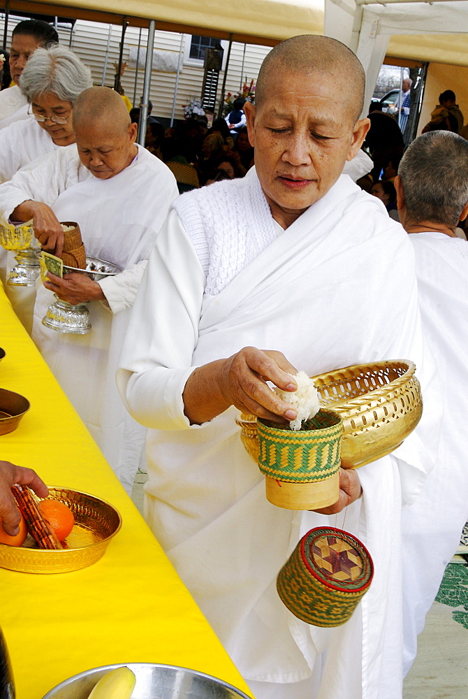 A LAotian-American female monk with shaved head makes an offering of rice during  worship as the  Laotian American community celebrates the Buddhist new year by gathering at a property in suburban East Hartford Connecticut on April 28, 2007. Several shrines are set up on the property. The celebrants leave offerings of food, flowers and money, pray, dance, and feast for a day. Immigrants from Laos, including the  Hmong people,  are refugees from the Vietnam War era, when they helped United States in the war.