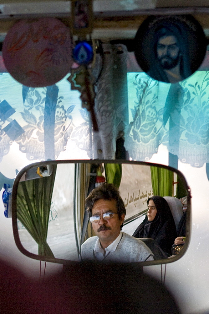 Dasht e Kavir, Iran - February, 2008: Bus driver and female passenger dressed in black reflected in the mirror of a bus enroute through the desert from Esfahan to Khur in Central Iran.