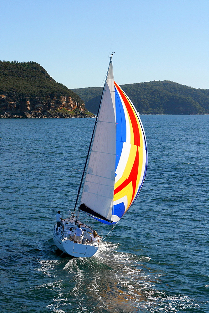 Aerial view of a sailing yacht with a colorful spinnaker cruising in Pittwater on the North Shore from Sydney, Australia.