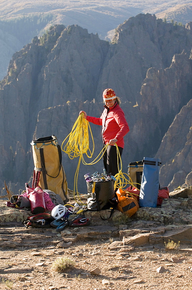 A woman coiling a climbing rope next to multiple bags of gear in the mountains of Crawford, Colorado.