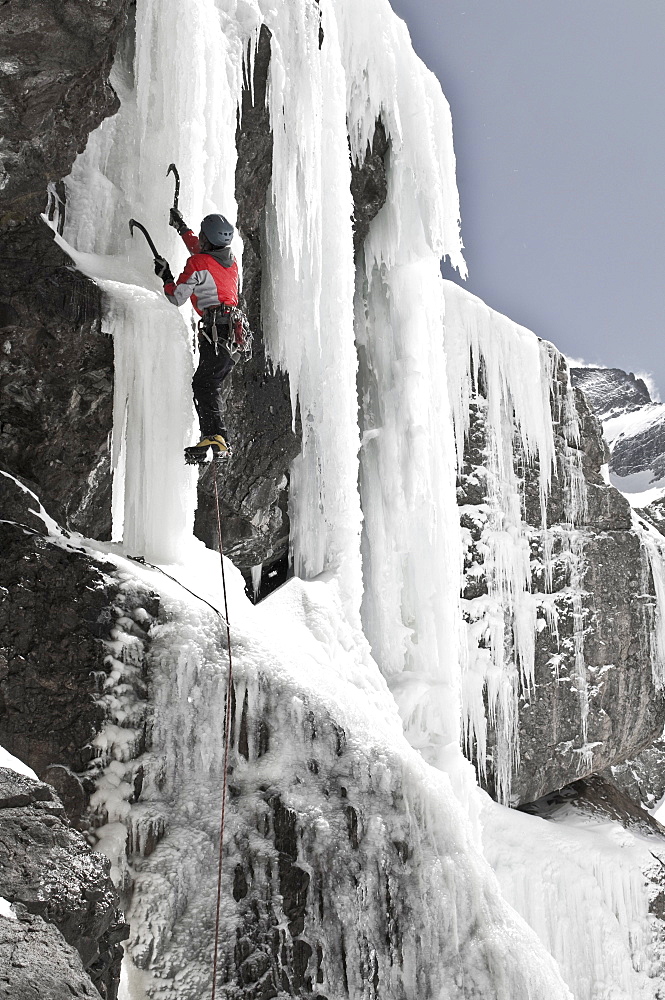 A woman ice climbing up a frozen waterfall at Willow Lake in the Sangre De Cristo Mountains, Crestone, Colorado.