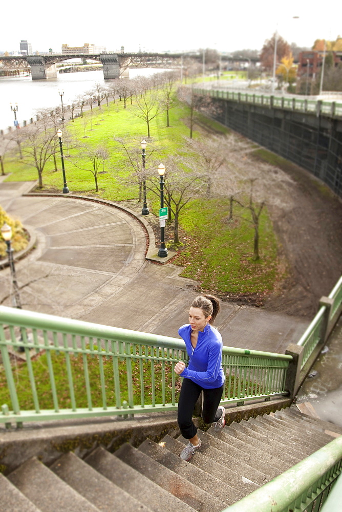 An athletic female in a blue jacket jogging stairs along the Portland, Oregon waterfront.