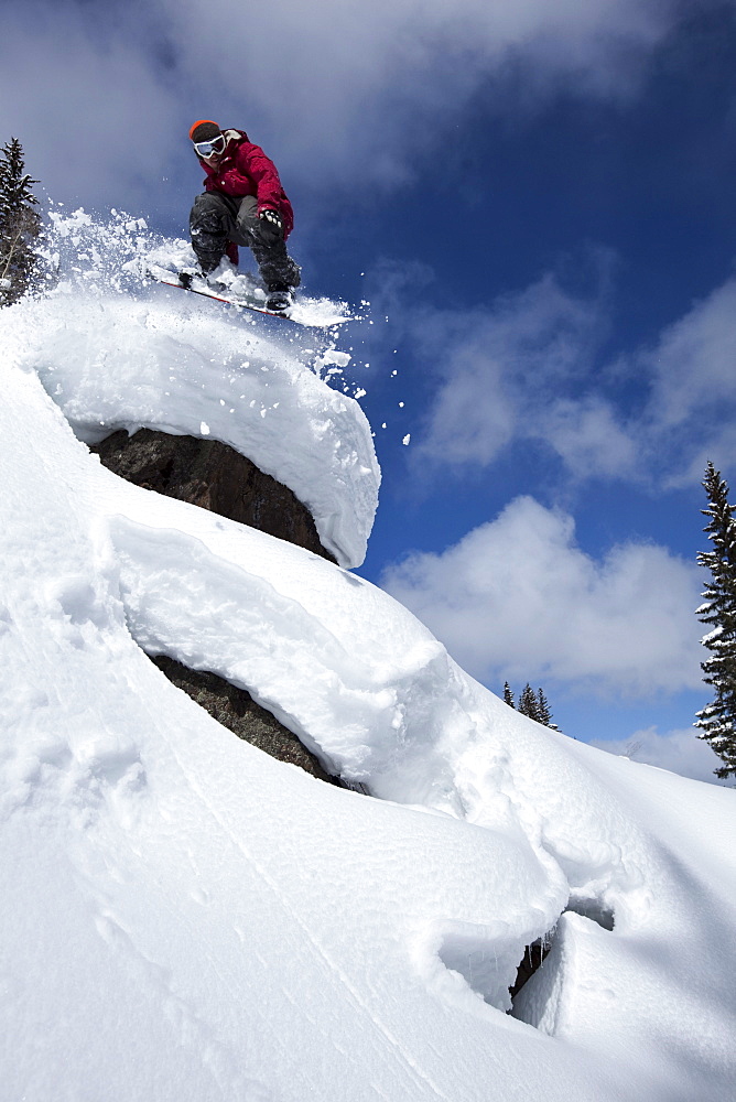 Young adult snowboarding off powder pillows in Colorado.