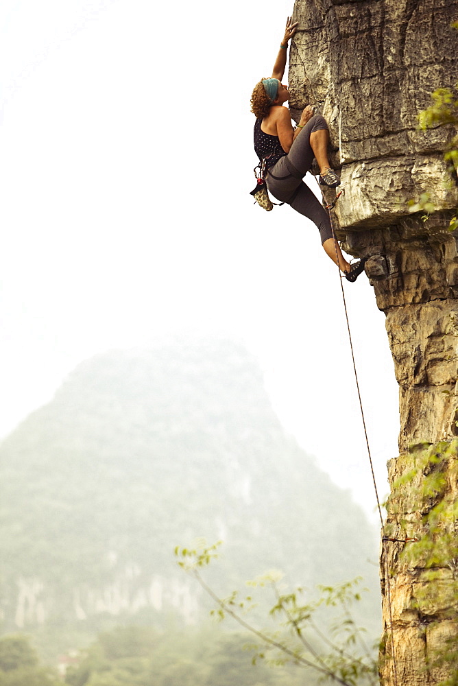 Female climber reaching out for a distant hold on overhanging limestone in China.