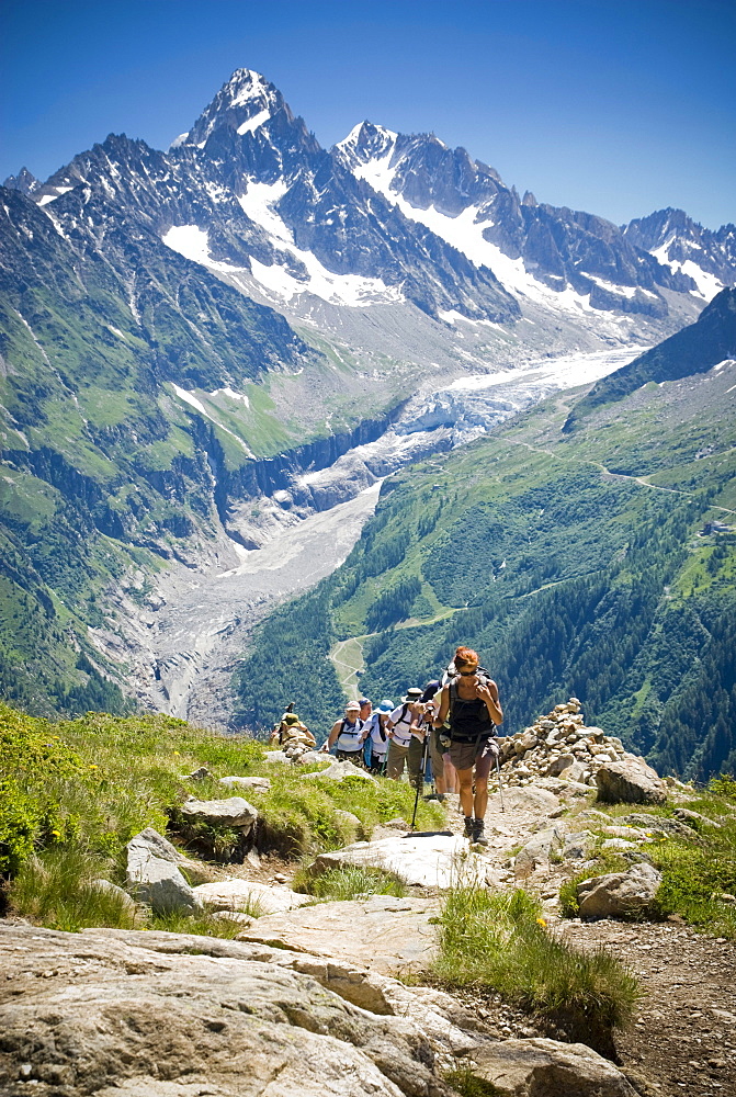 Hikers trek up a hill as the majesty of the Alps towers in the background.