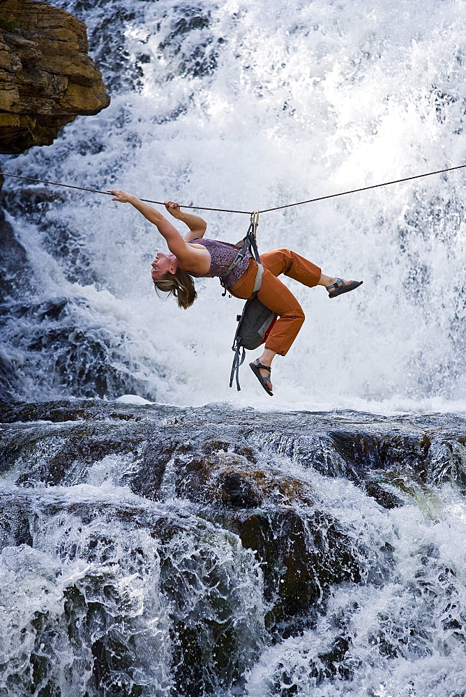 A woman crosses a waterfall using a Tyrolean Traverse on a rope.