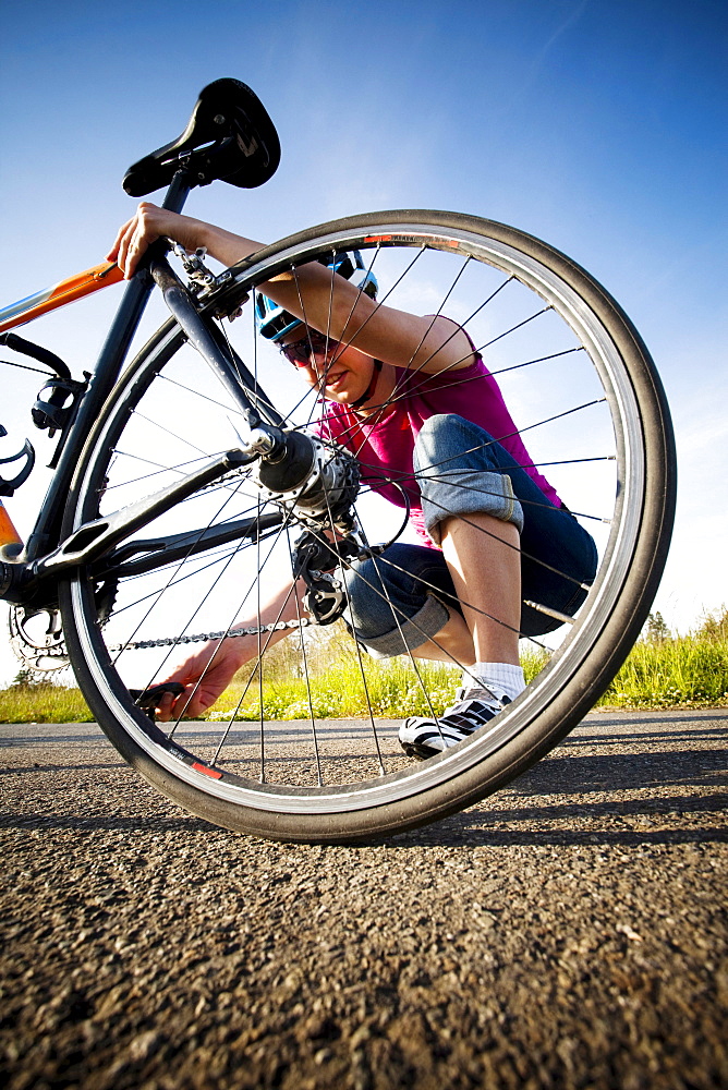 A young woman inspects her chain and back tire on the way home from work on her commuting bike.