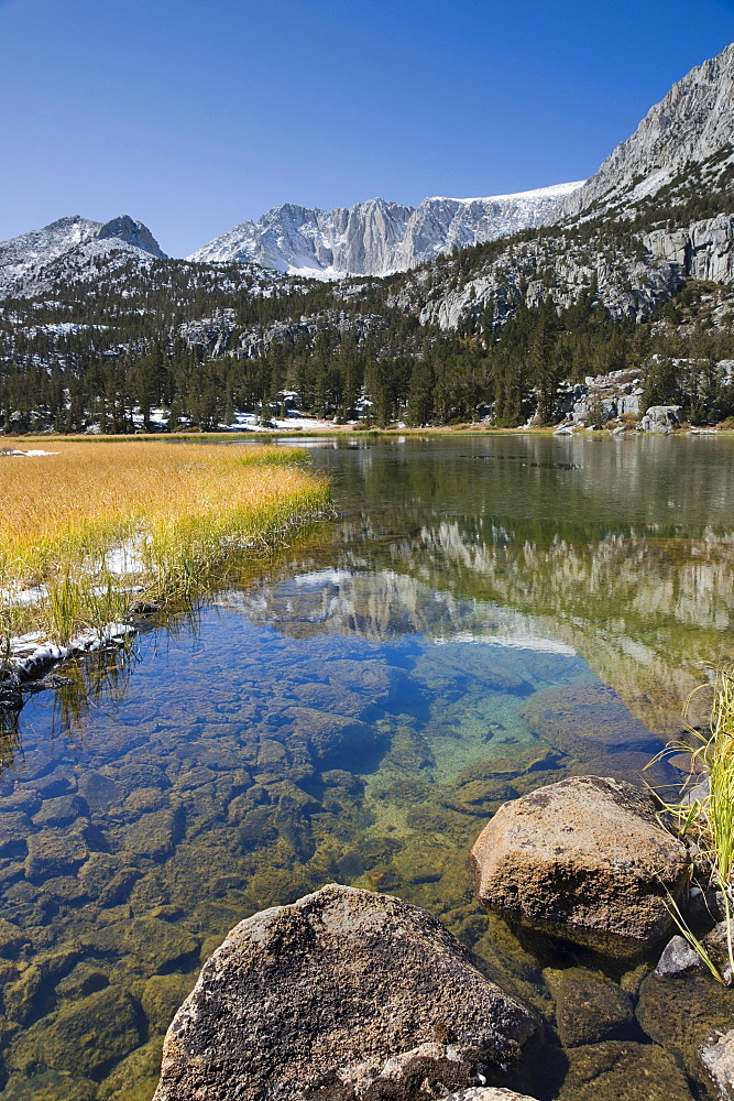 The High Sierra mountains with new fall snow reflecting in an alpine lake in Rock Creek Canyon in California