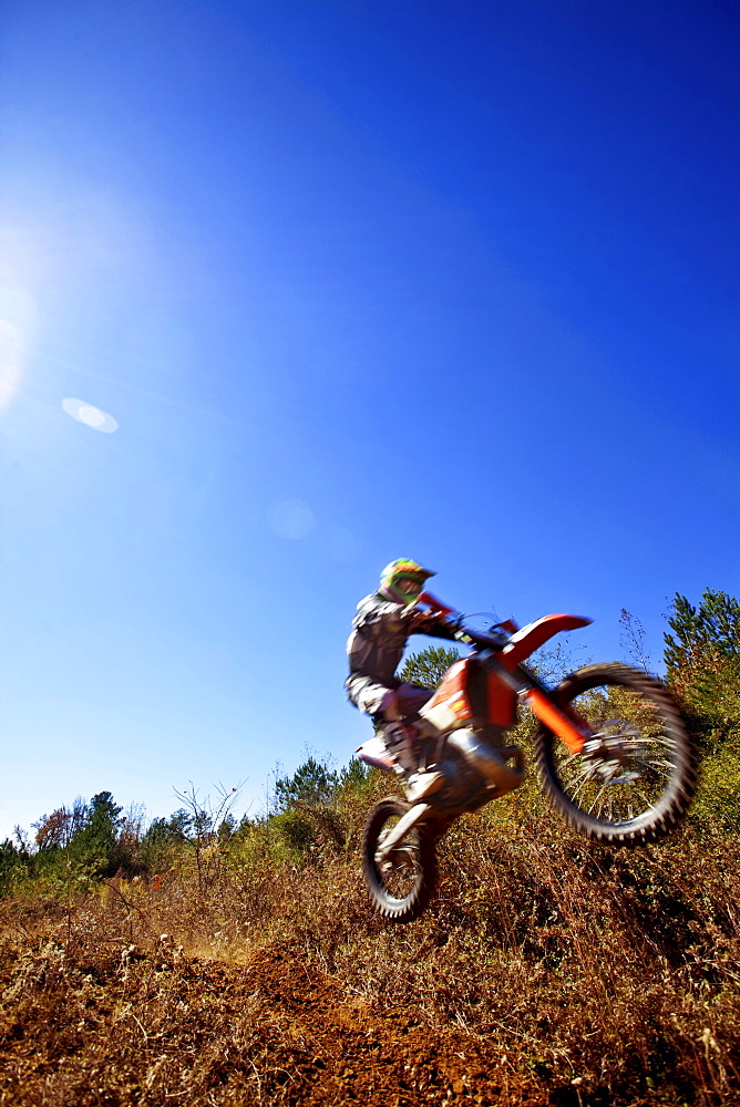 A motorcyclist catches air on a jump during an Enduro race in Maplesville, Alabama. (Back lit, Lens Flare, Motion Blur)