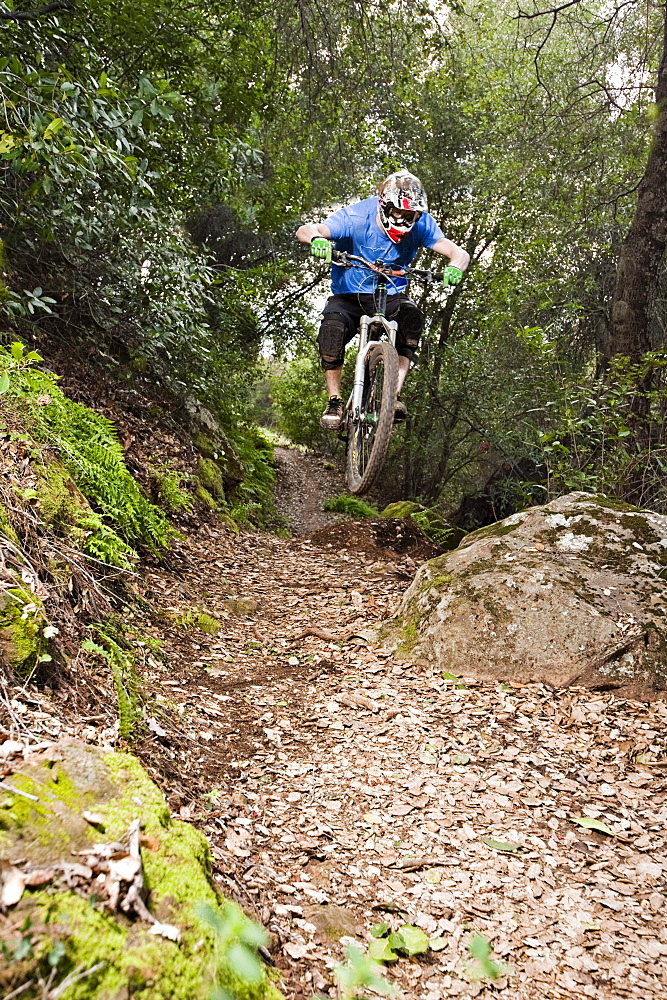 A young man rides his downhill mountain bike on Knapps Castle Trail, surrounded by beautiful scenery in Santa Barbara, CA.