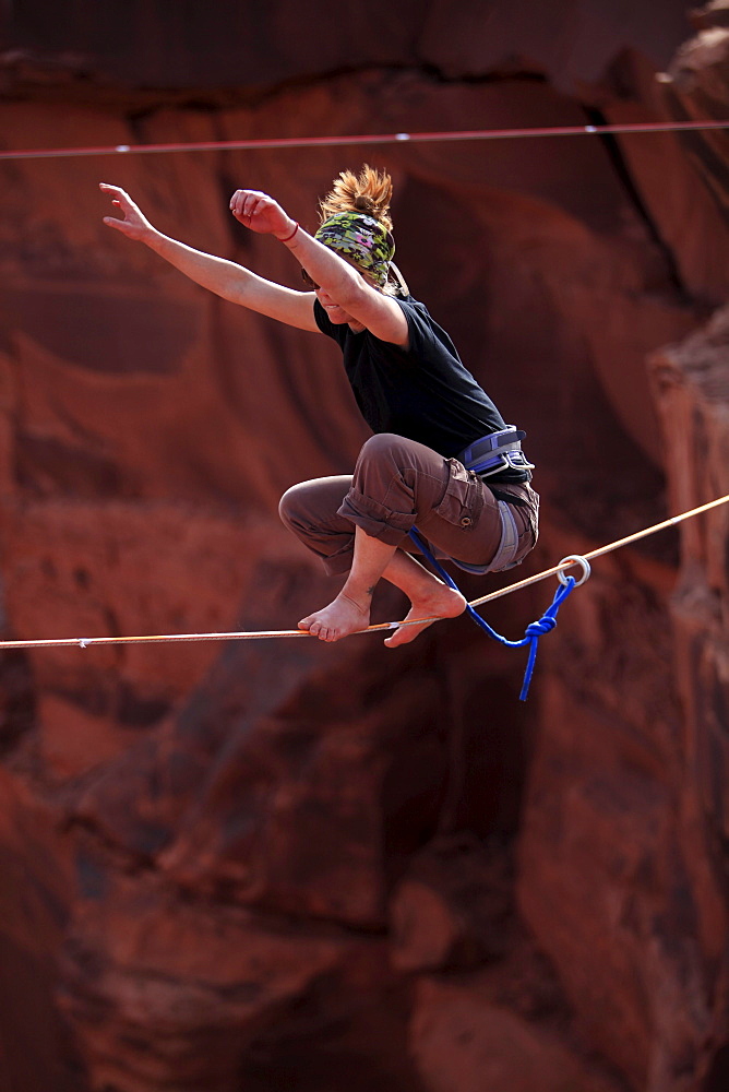 A female highliner stands up on a highline at the Fruit Bowl in Moab, Utah, USA.