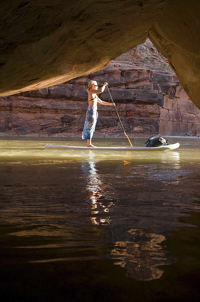 Woman on paddle board in front of cave while rafting down the Lower San Juan River, Mexican Hat, Colorado.