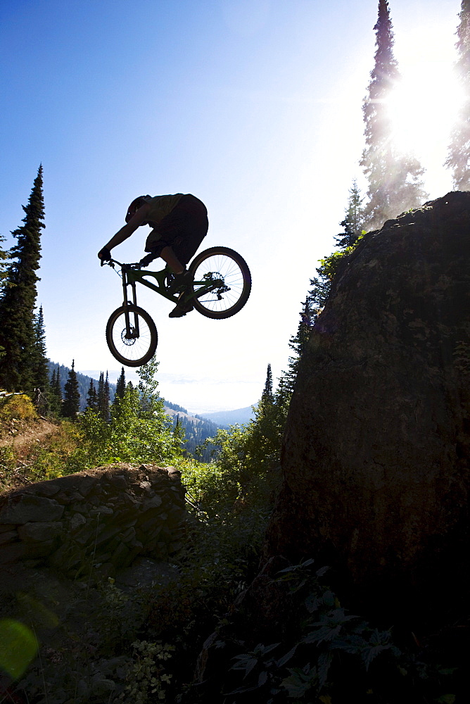 A athletic man mountain biking jumps off a large cliff while downhilling on Teton Pass in Jackson, Wyoming.