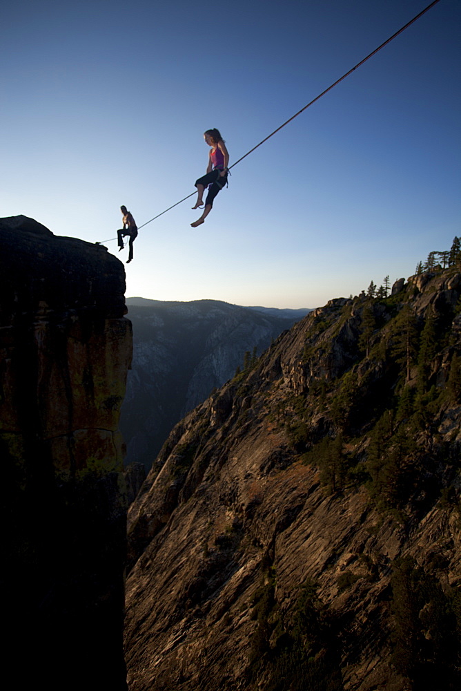 Female highliners simultaneously sitting on a highline above the Yosemite Valley floor at Taft Point, Yosemite National Park, California, United States