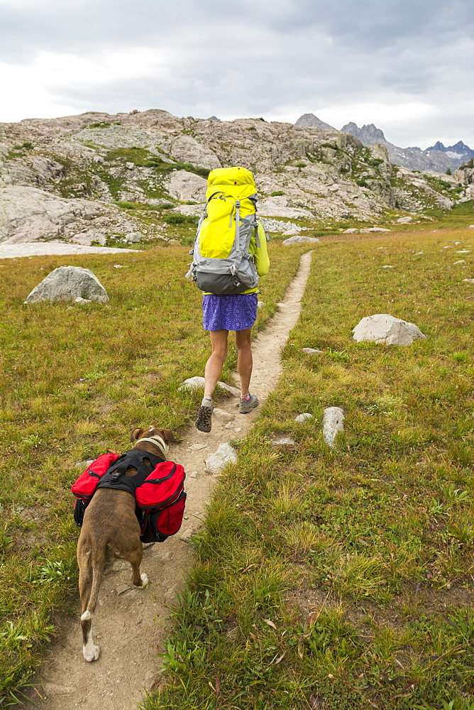 A woman and her dog hiking along trail into Titcomb Basin in the Wind River Range, Bridger Teton National Forest,  Pinedale, Wyoming.