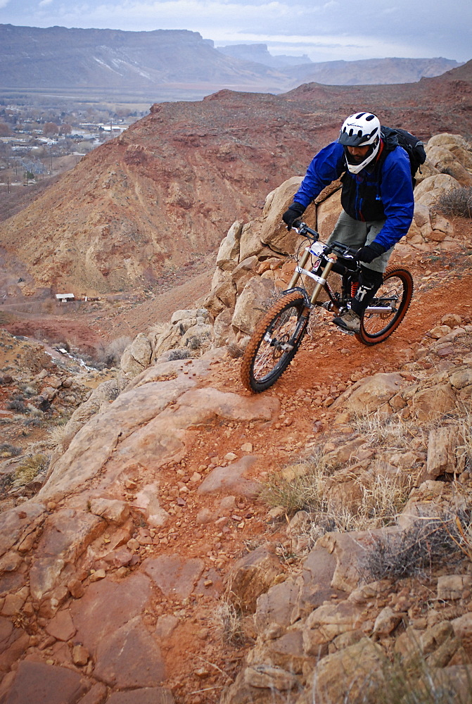 Experienced riders descend a downhill mountain bike trial which drops into the town of Moab, Utah.