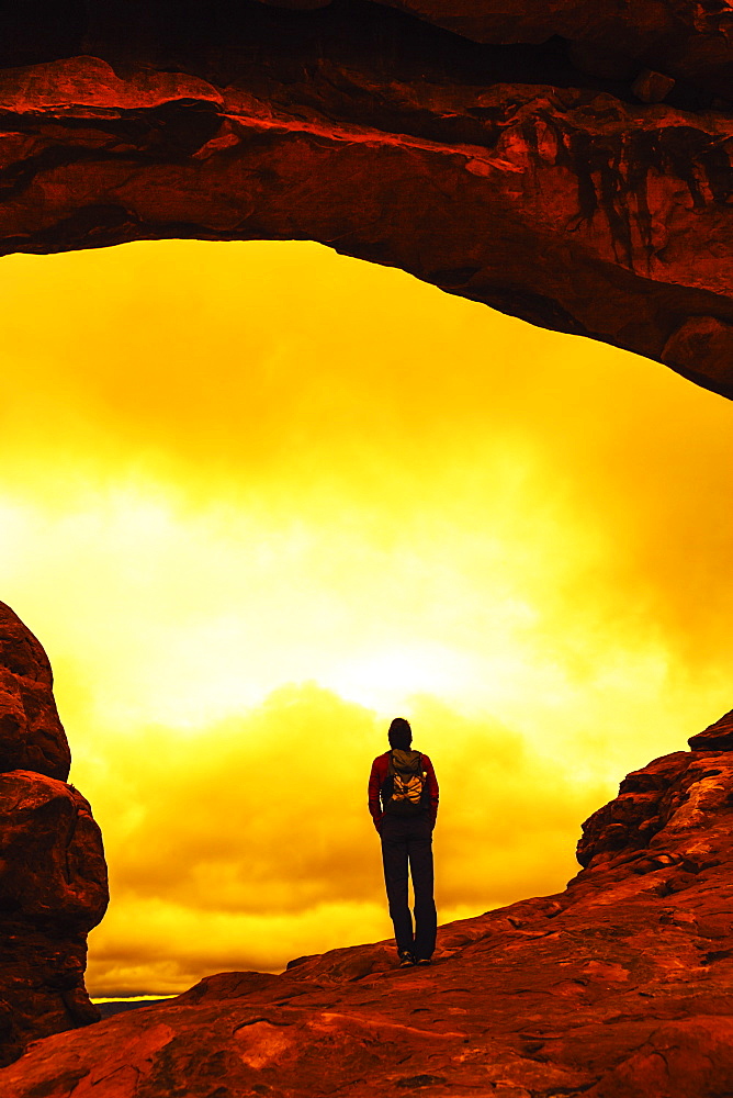 Rear view of a female hiker as she stands under a natural arch in Arches National Park.