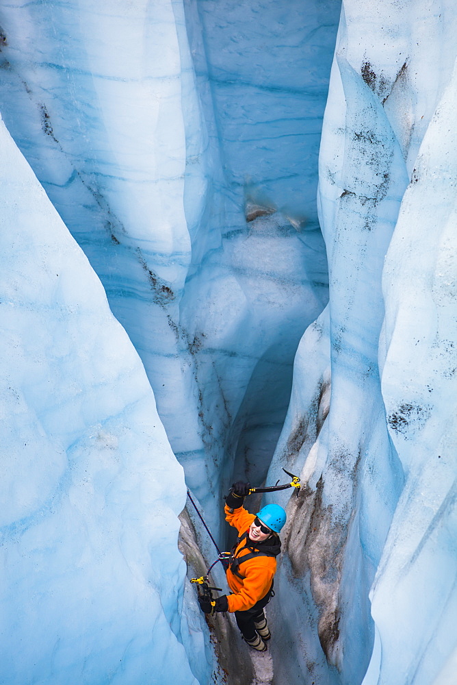 A woman swings her ice tools as she prepares to climb out of a moulin on a day trip with St. Elias Alpine Guides to the Root Glacier in Wrangell-St. Elias National Park, Alaska.