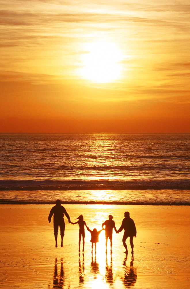 A family walks hand-in-hand at sunset on Pacific beach.