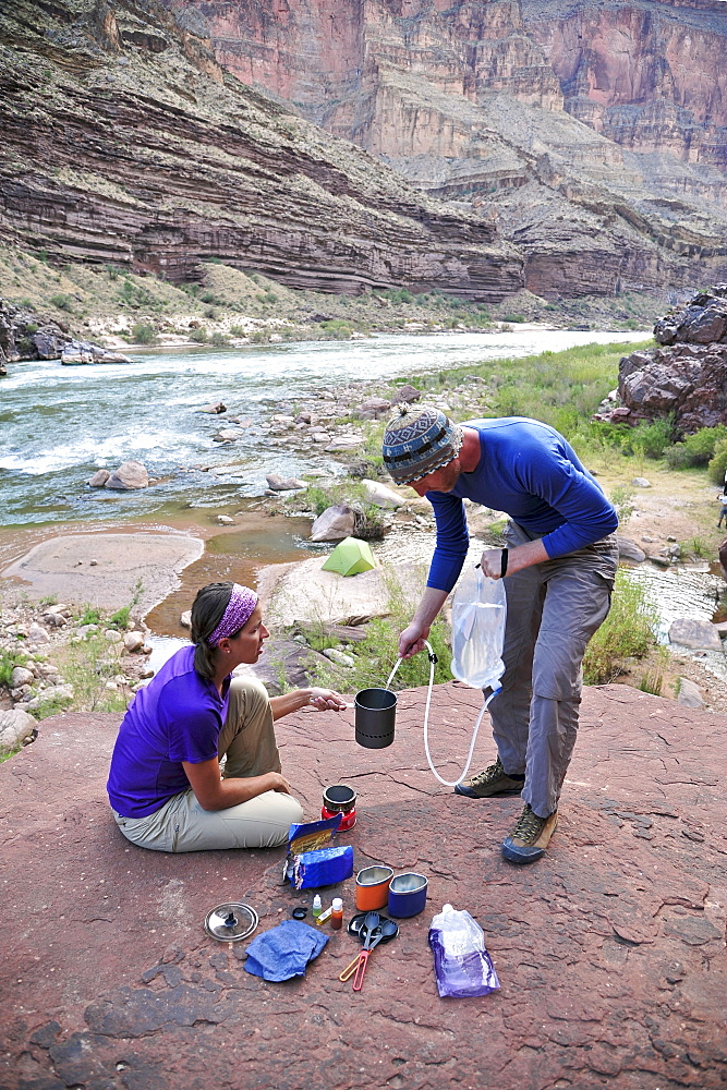 Hikers cook dinner on a cliff-pinched patio above camp and the Colorado River near Deer Creek Falls in the Grand Canyon outside of Fredonia, Arizona November 2011.  The 21.4-mile loop starts at the Bill Hall trailhead on the North Rim and descends 2000-feet in 2.5-miles through Coconino Sandstone to the level Esplanada then descends further into the lower canyon through a break in the 400-foot-tall Redwall to access Surprise Valley.  Hikers connect Thunder River and Tapeats Creek to a route along the Colorado River and climb out Deer Creek.