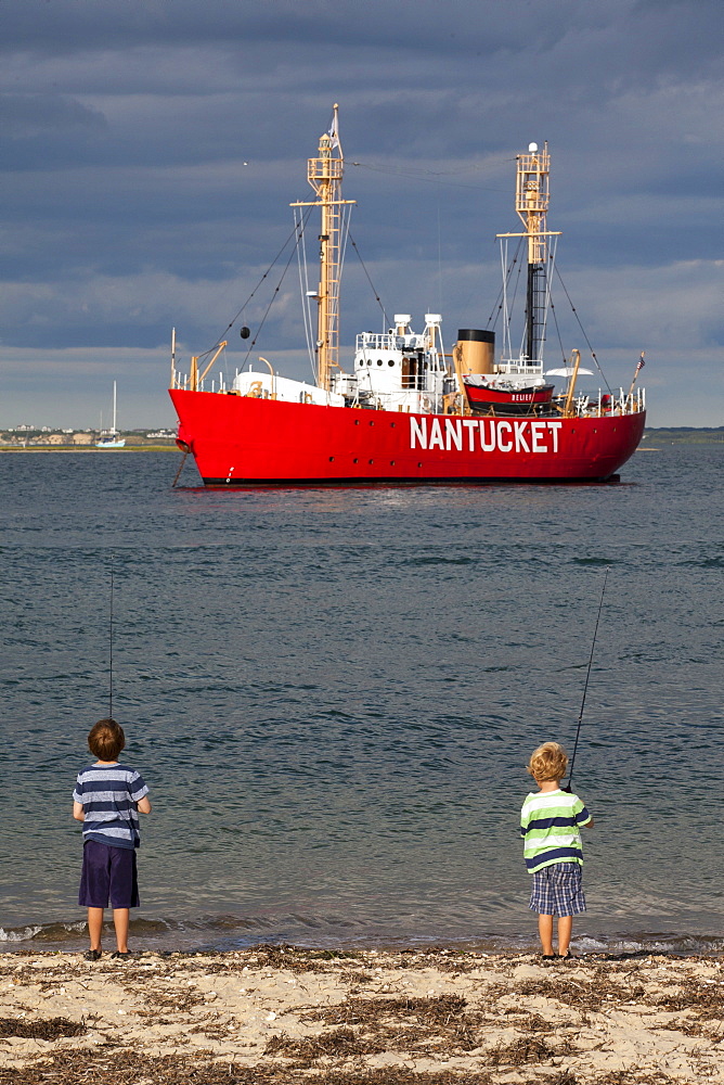 Two young boys fish at Nantucket's Brant Point Lighthouse.  In the background is Nantucket's Lightship which also helps steer boats safely into and out of Nantucket's harbor.