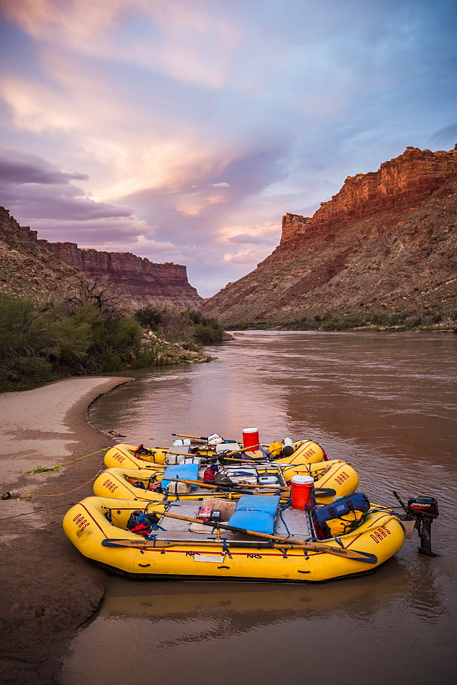 Inflatable rafts sit on the shore at sunset along a river.