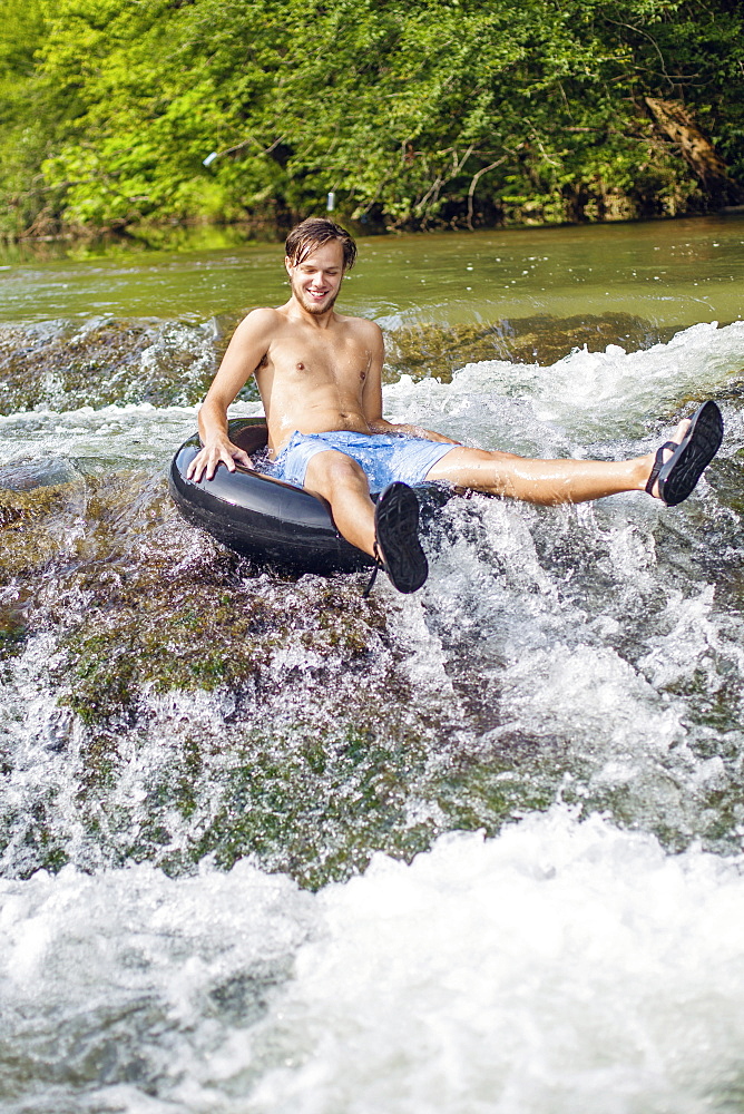 A young man tubes down rapids on a river.
