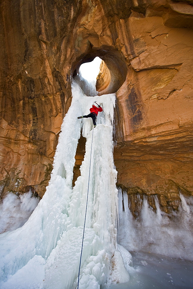 A man ice climbing a frozen waterfall through a sandstone arch in Utah.