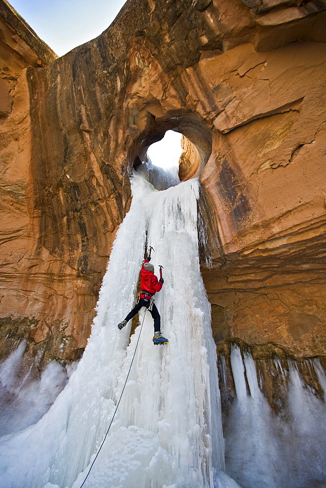 A man ice climbing a frozen waterfall through a sandstone arch in Utah.