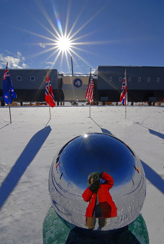 A man photographs himself in the reflection of the South Pole memorial pole.