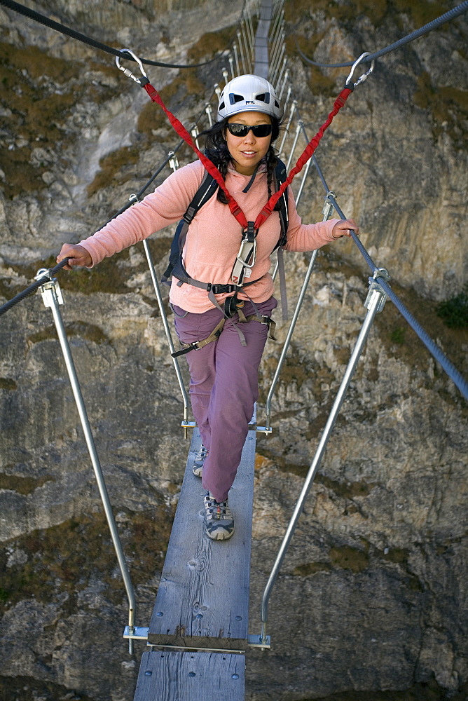 A young woman walking on a bridge while engaging in the sport of Via Ferrata in Val D'isere, Savoie, France.