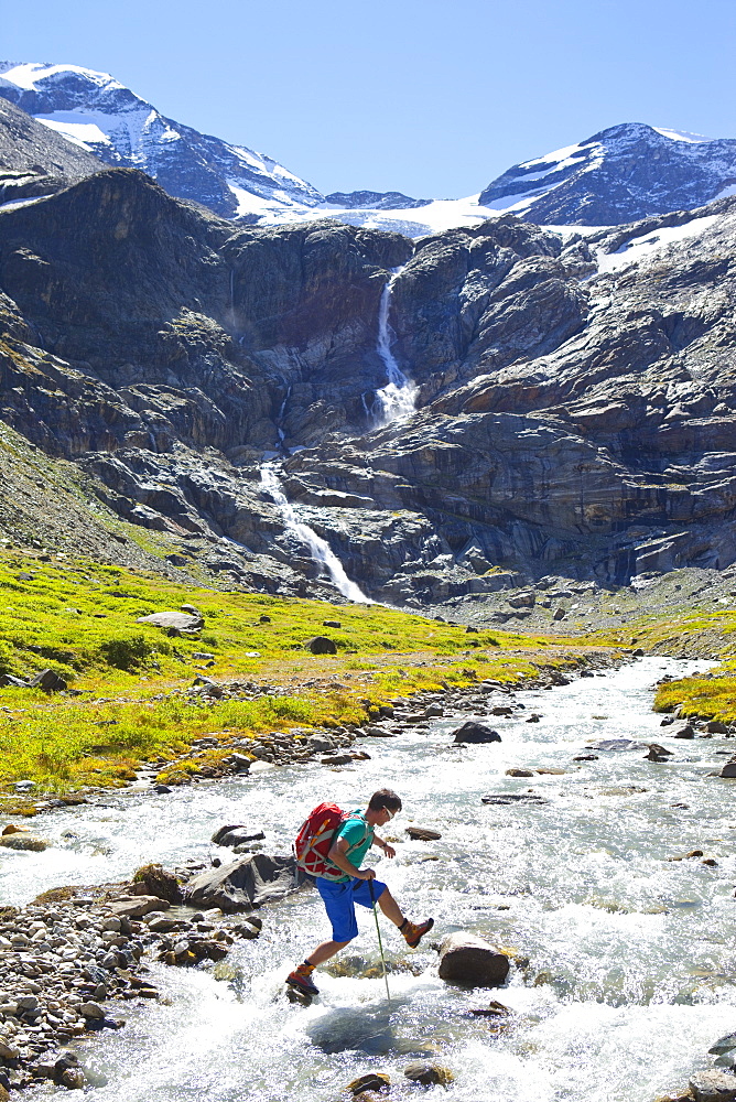 A male hiker jumping from stone to stone to cross a river, during the Glocknerrunde, a 7 stage trekking from Kaprun to Kals around the Grossglockner, the highest mountain of Austria.