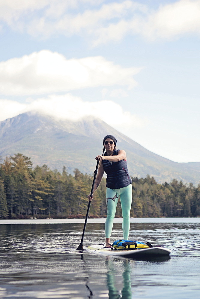 A young woman paddle boards on a pond in Maine.