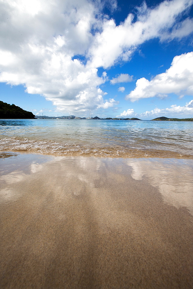 Stunning clouds, blue sky, sand and turquoise waters frame a line of boats anchored in Caneel Bay, St. John, US Virgin Islands.