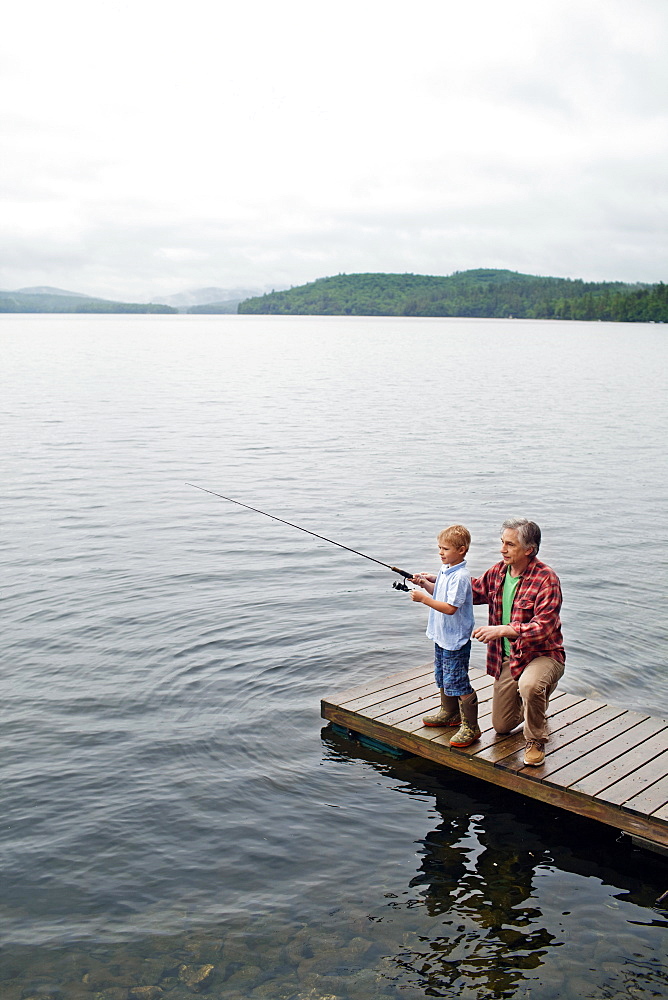 Senior man showing grandson how to fish off dock at Kezar Lake