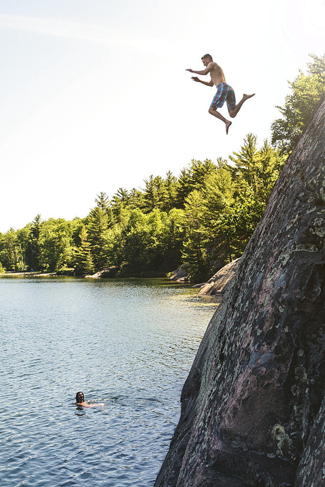 A Young Man Is Jumping Off A Cliff Into George Lake While Another Person Is Looking From Under