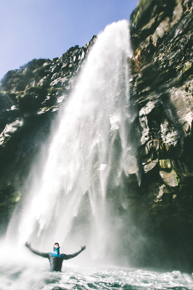 A Man In A Wetsuit Stands Under A Big Waterfall In The Faroe Islands