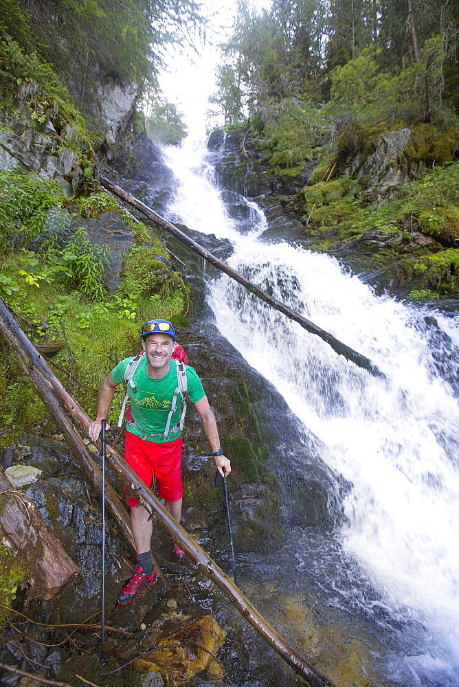 A Male Hiker Is Soaking Wet After Traversing A River With A Waterfall In The Val Danniviers