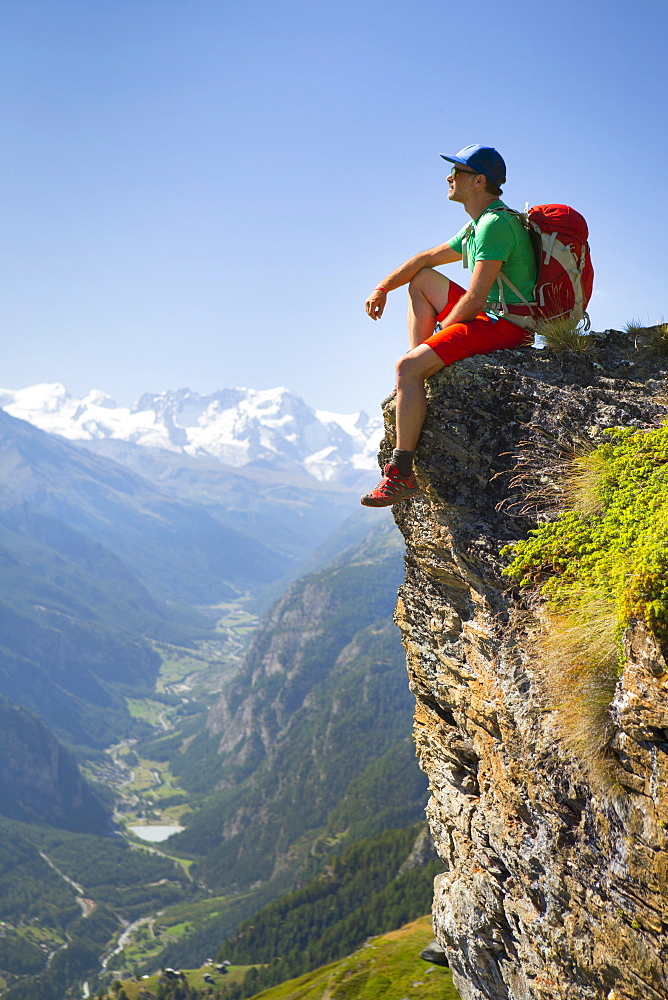 A Hiker Is Taking A Rest At A Steep Rock Face  Above The Matterhorn Valley