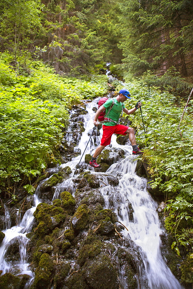 Male hiker stepping over mountain river stream in woods