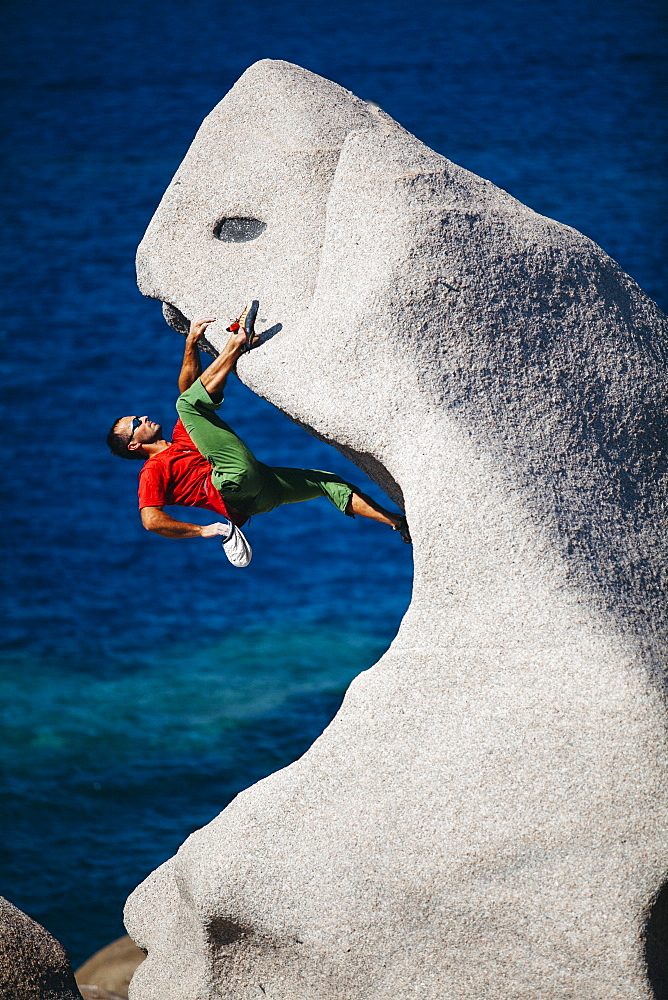 Man climbing on rock near sea, Capo Testa, Sardinia, Italy