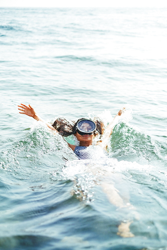 girl in a swimsuit and diving googles playing with the waves on the beach