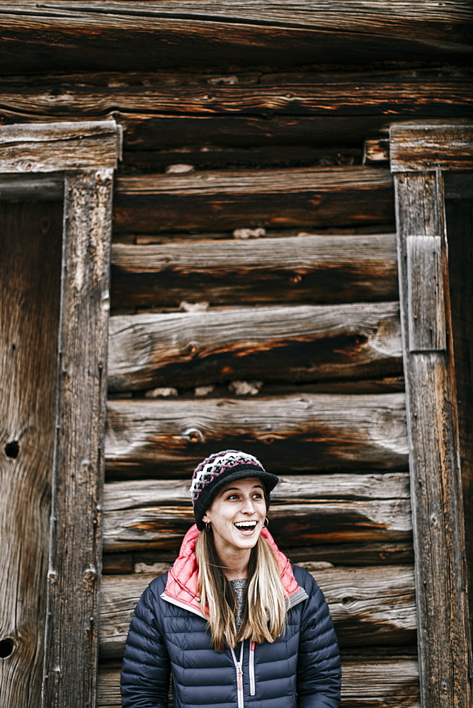 Waist up shot of smiling young woman in front of log cabin