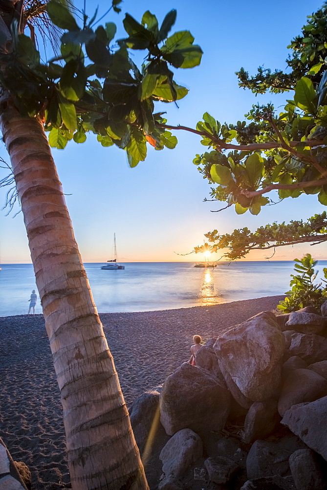 View of beach at sunset with palm trees, tourists and sailboat in distance, Black Sand Beach, Basse Terre, Guadeloupe