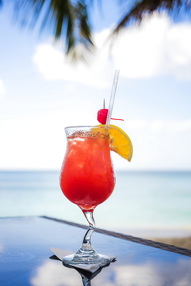 View of Caribbean tropical rum punch cocktail in glass on table against sea, Pink Gin Beach, Grenada