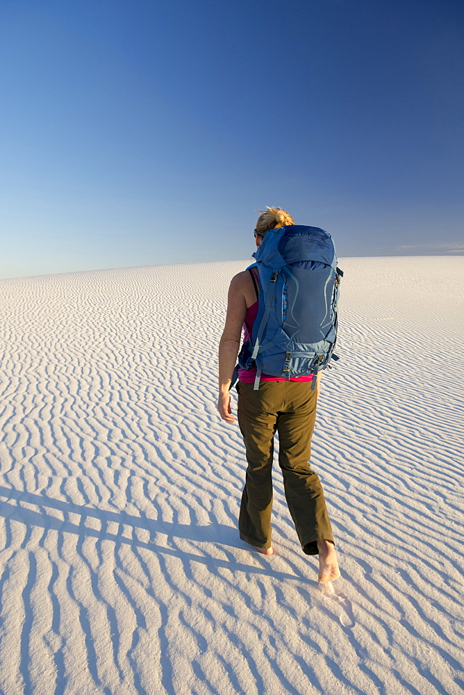 Rear view of female backpacker hiking in desert of White Sands National Monument, Alamogordo, New Mexico, USA